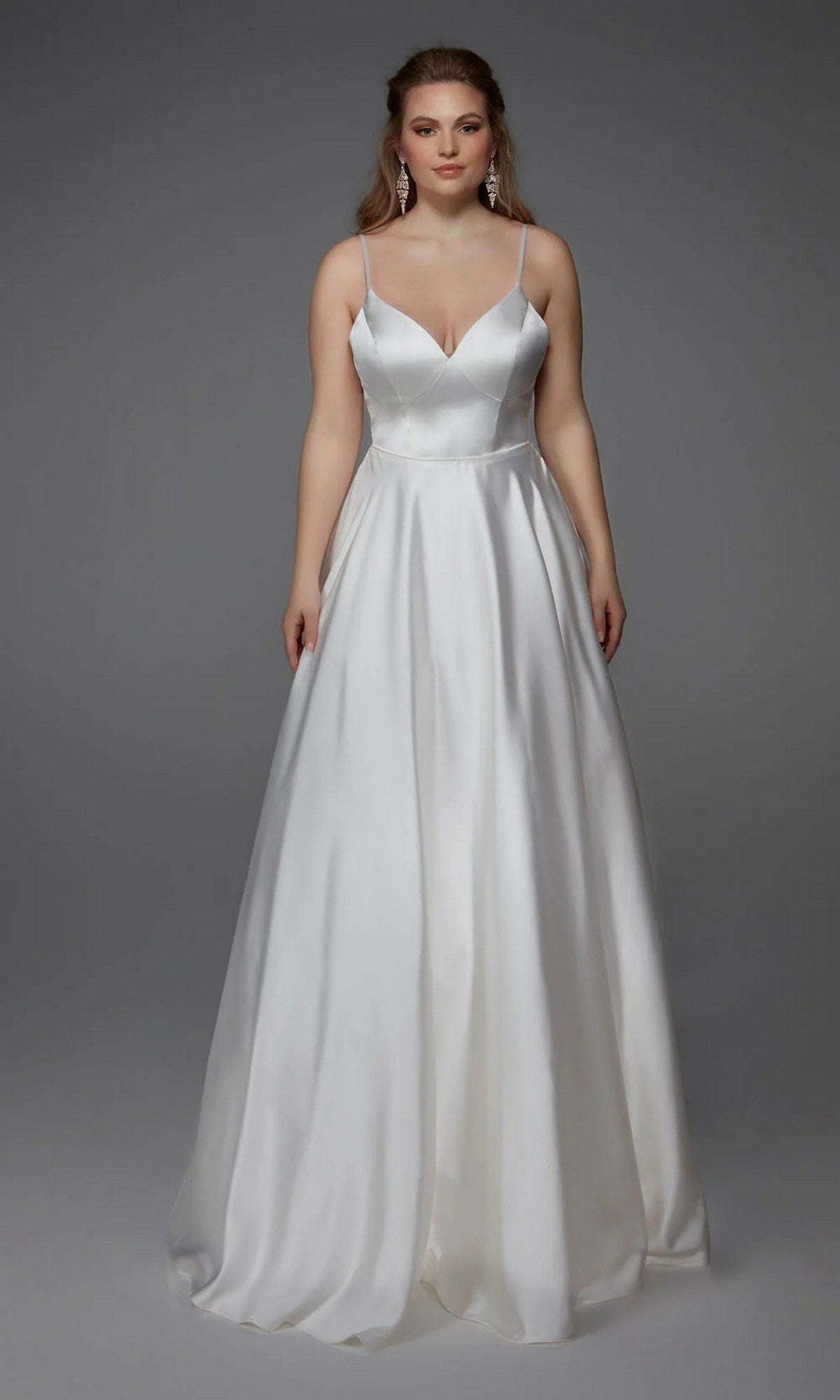 A woman faces forward against a plain gray background, wearing the Long White Dress: Alyce 7009 in Diamond White—a floor-length satin bridal gown with thin straps and a deep V-neckline.
